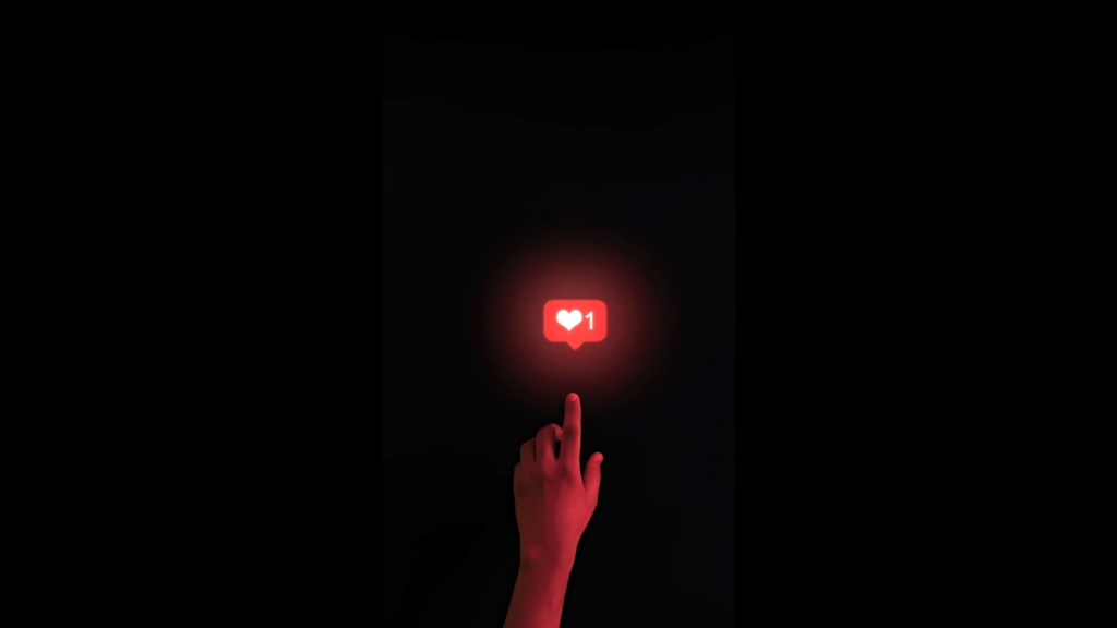 A hand illuminated by a red light holds a finger pointing a like emoticon with a heart