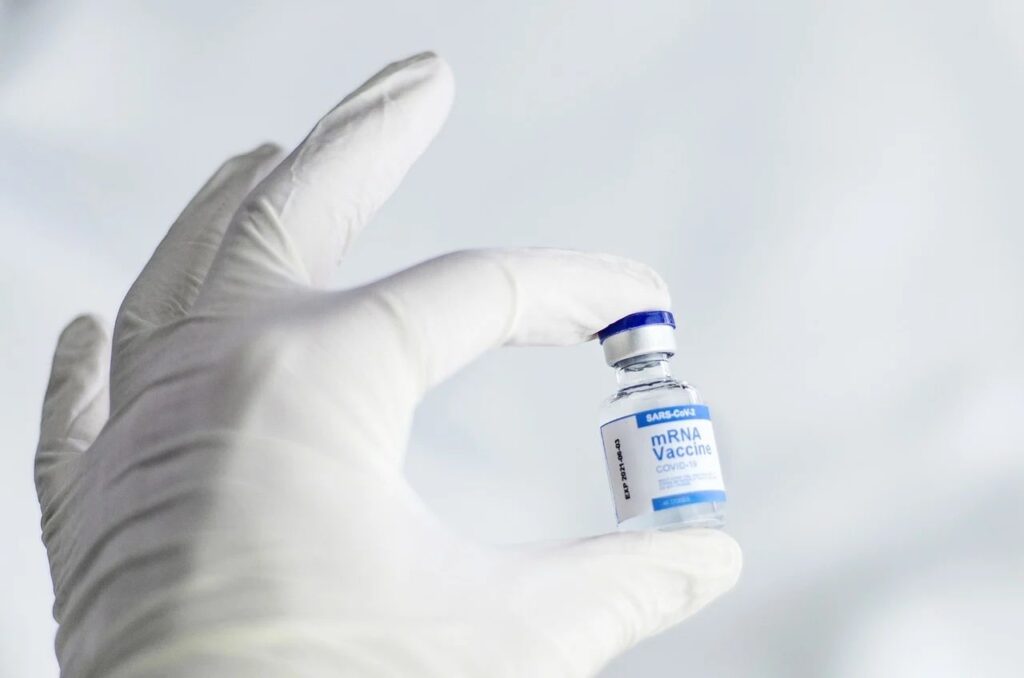 A hand with white gloves holding a jar containing a COVID-19 vaccine
