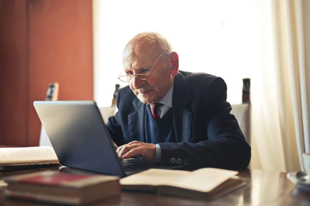 Elder man looks concentrated while looking and typing on a laptop.