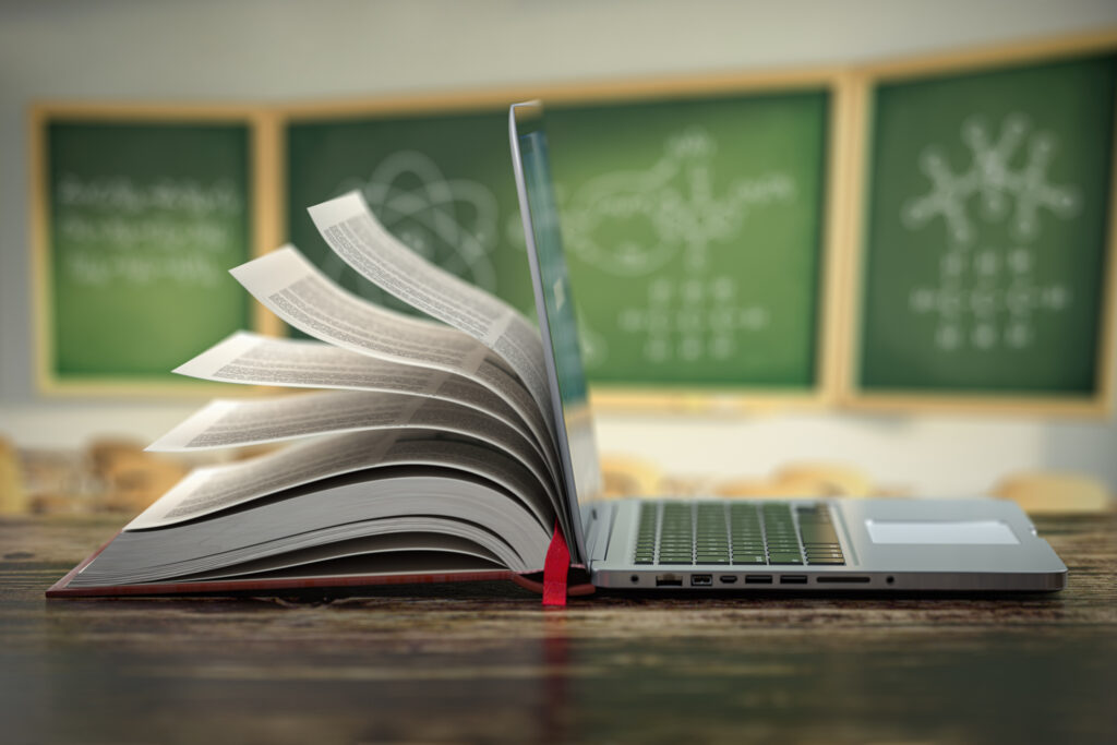 Half a book and laptop lay on a desk in a classroom.
