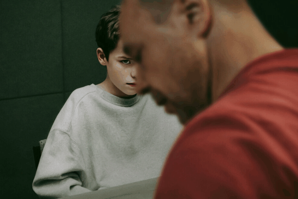 Teen looks at camera menacingly, while an adult's profile is seen on the foreground.